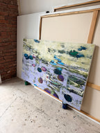 Side view of a large-format original textured water lilies painting in an artist's loft studio. The single-edition canvas artwork by Ukrainian artists is placed on the floor next to a rustic red brick wall, highlighting its authentic hand-painted texture.
